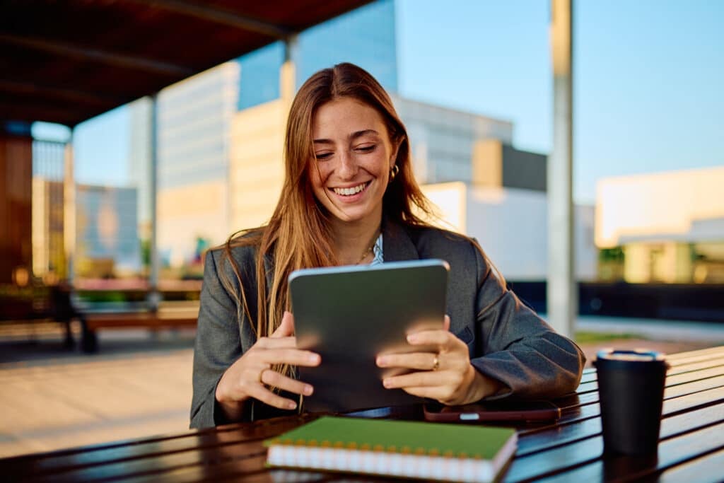 Smiling professional in a blazer reviewing a tablet at an outdoor table in a modern business district